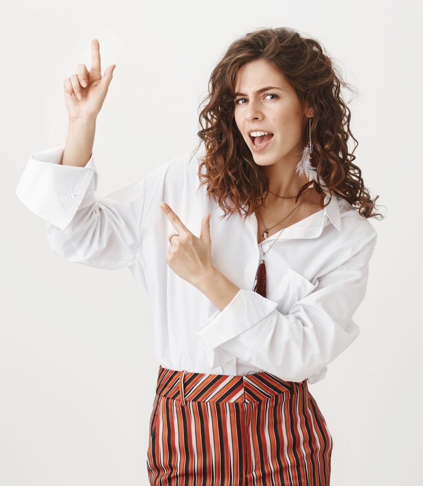 Yeah look here. Portrait of confident good-looking european woman with curly hair, gazing self-assured at camera while pointing up with finger gun gesture, giving great advice or suggestion. Advertisement concept